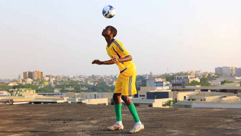 A soccer player is on the roof and kicks the ball with his head